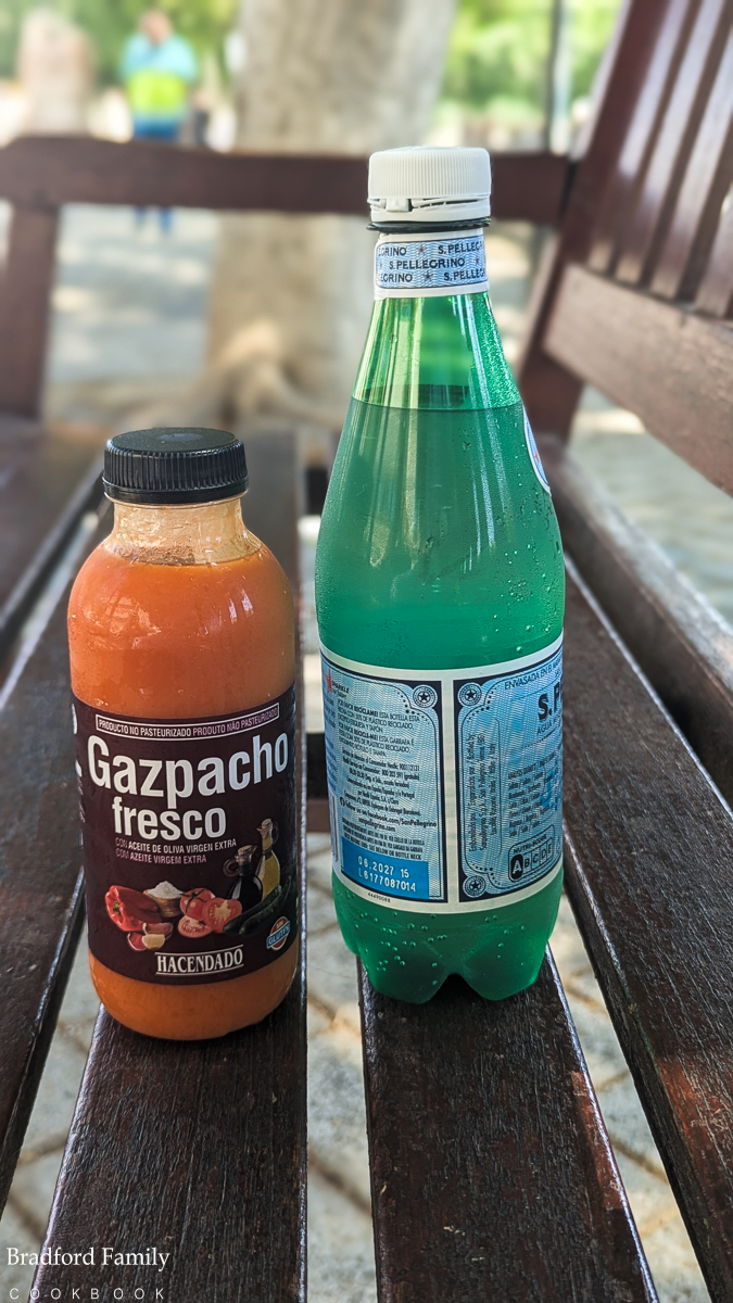 A paciture of a bottle of shop-bought gazpacho and a bottle of San Pelligrino water on a bench in the shade in Murcia